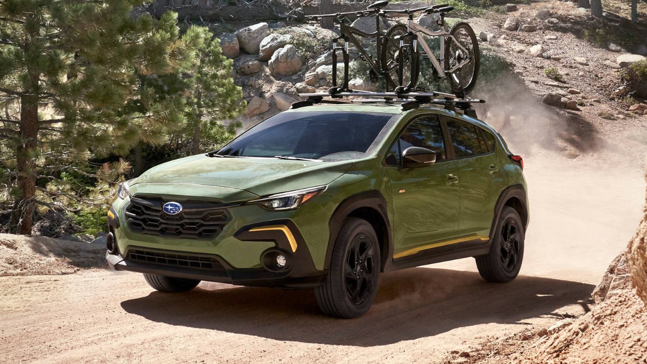 Vue avant trois quarts du Subaru Crosstrek 2025 vert en action sur un chemin de terre, avec vélos fixés sur le toit.