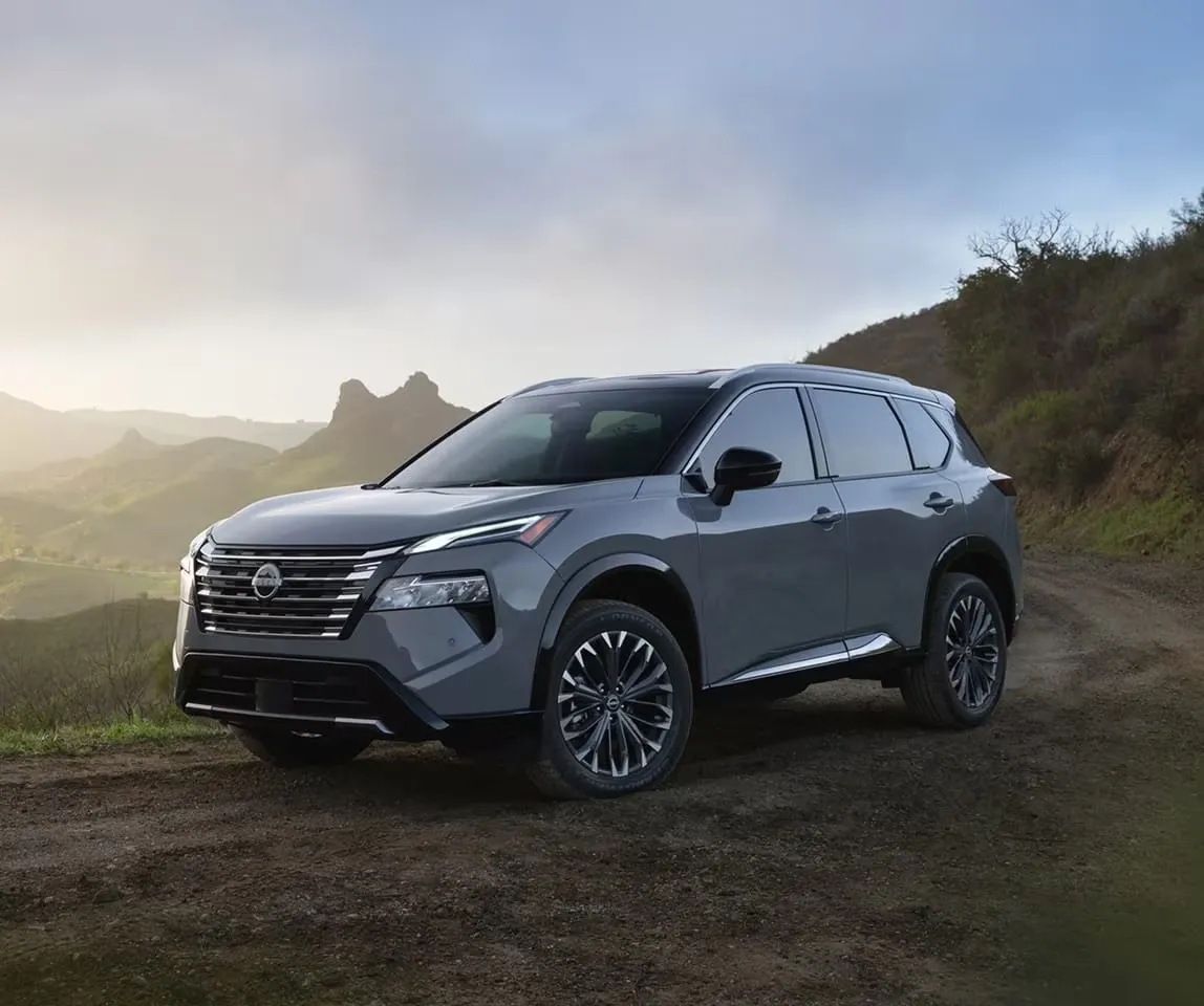 Vue avant du Nissan Rogue 2026 gris argenté stationné sur un chemin de campagne au lever du soleil, mettant en valeur son nouveau design robuste et moderne.