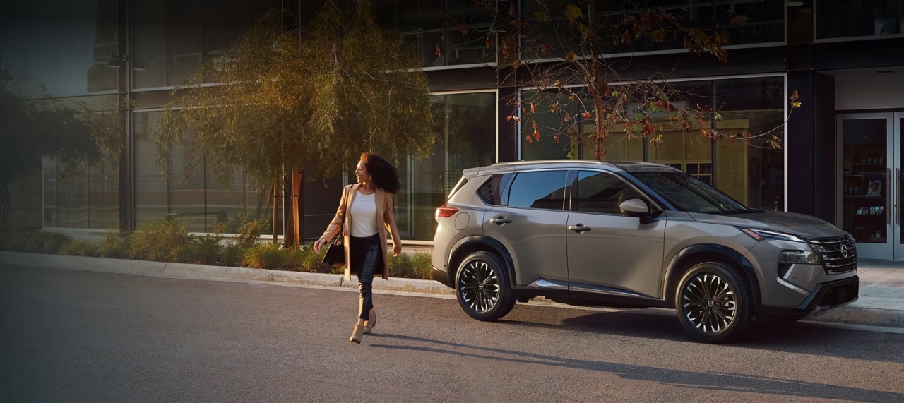 Femme marchant vers un Nissan Rogue 2026 stationné devant un immeuble moderne, illustrant le style urbain et élégant du VUS.